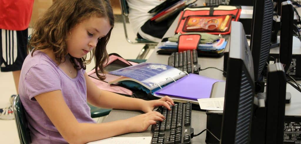 An elementary school student looking at her notes while using a computer
