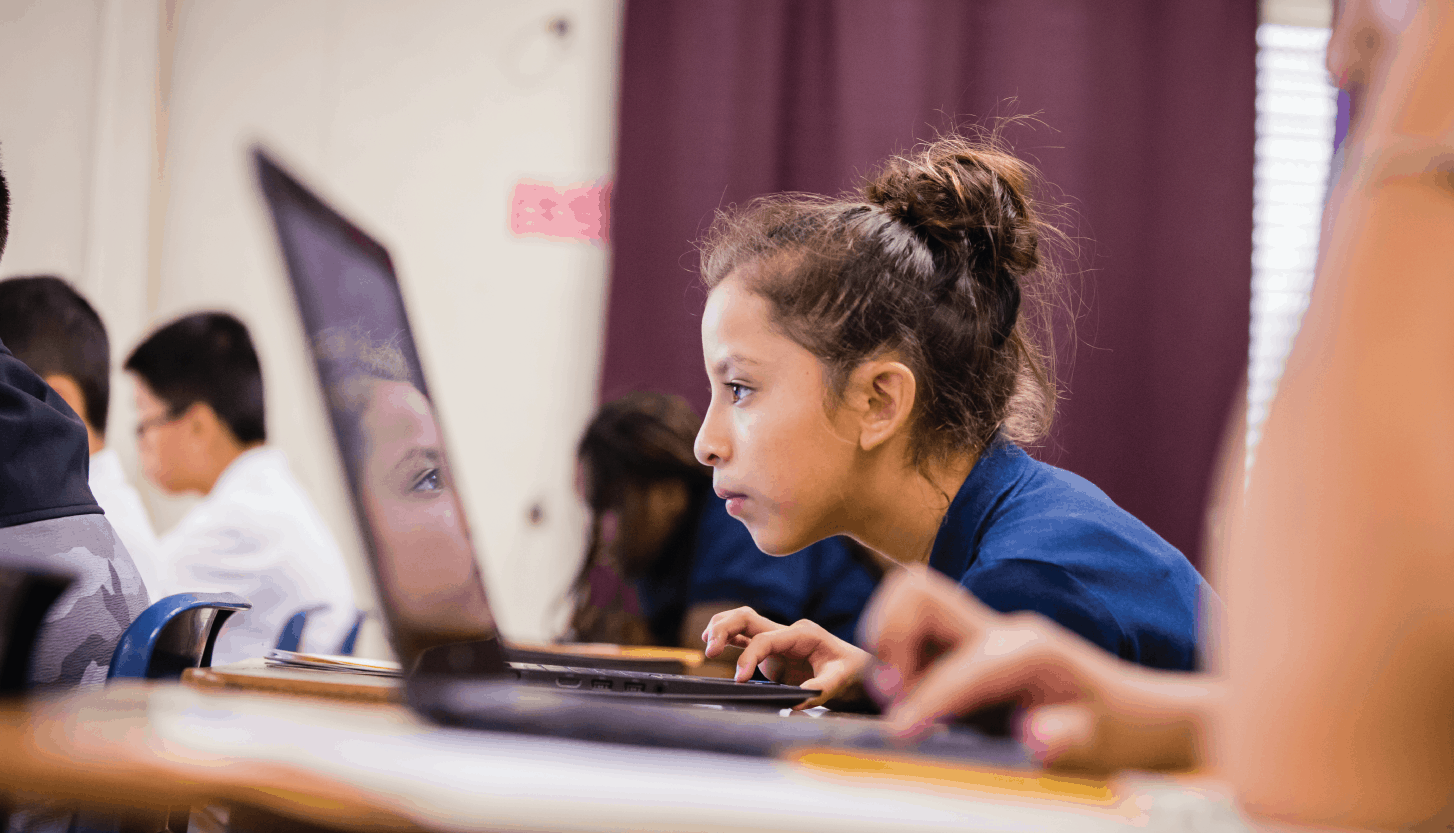 Image of a girl in a classroom focusing on what is on her computer screen