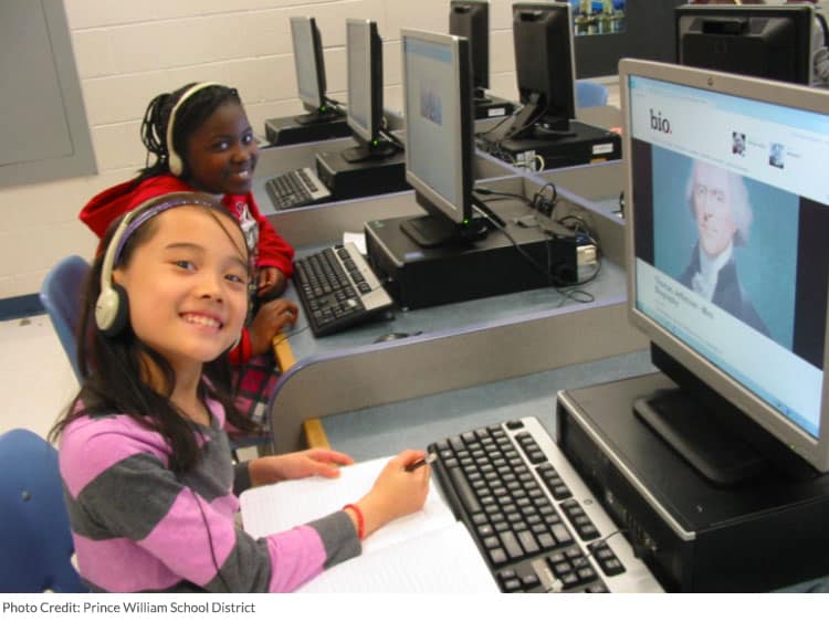 Kids on a computer with headphones smiling at camera