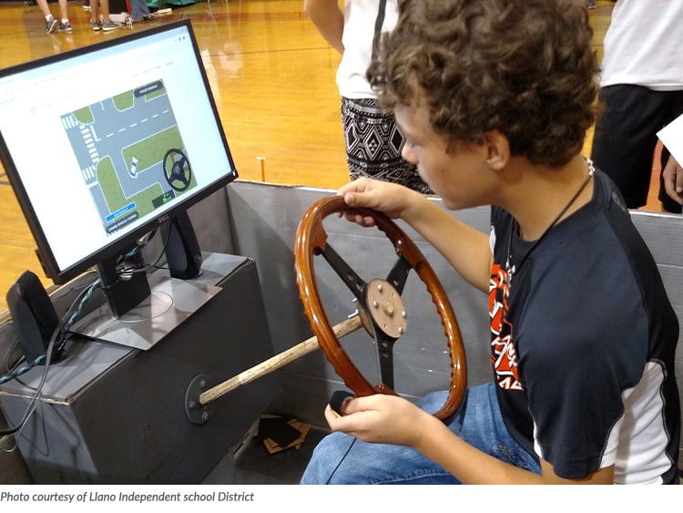 Photo of a boy in a simulator car watching a graphic on a computer monitor
