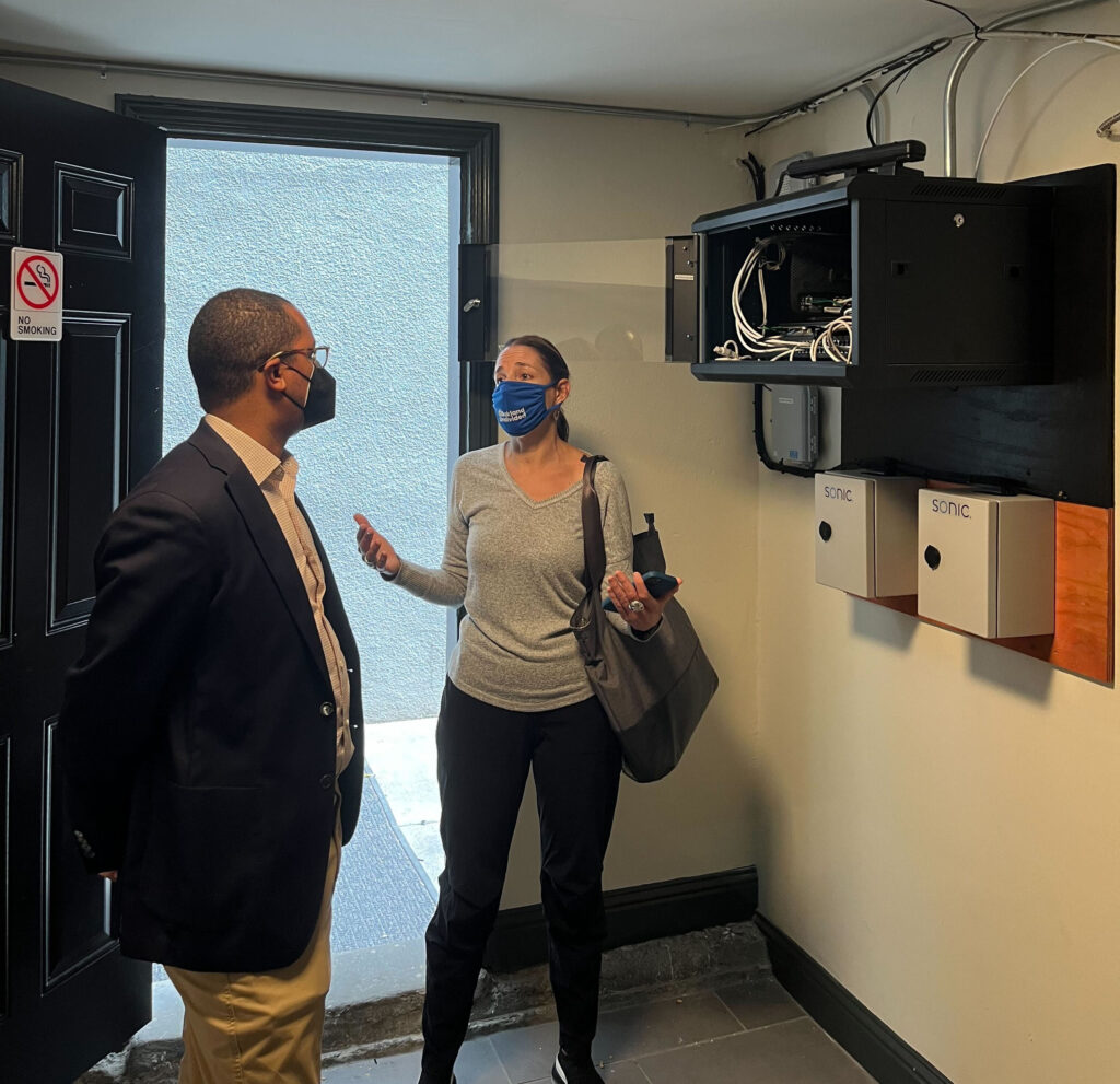 EducationSuperHighway’s Oakland General Manager Stephanie Silver and FCC Commissioner Geoffrey Starks at a building recently connected through the Free Apartment Wi-Fi program. Silver is pictured showing Starks the Wi-Fi set up for the building.